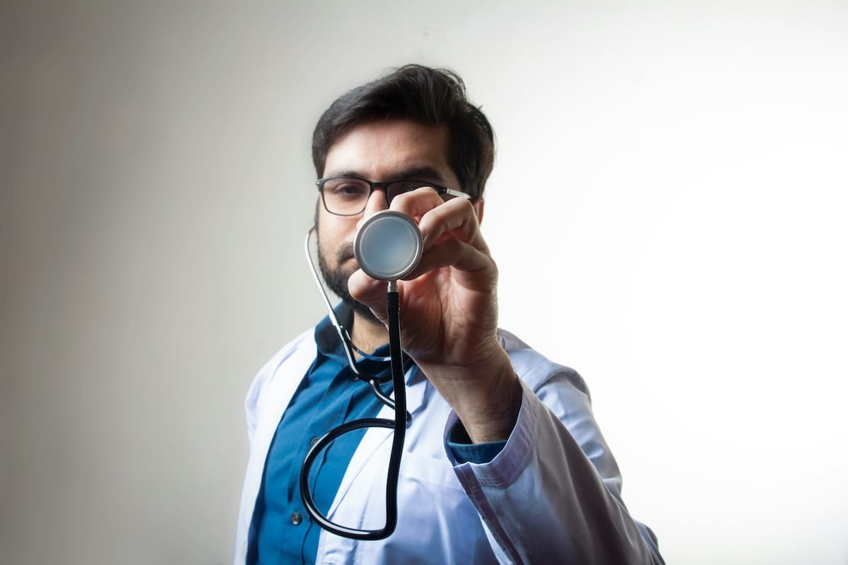 Individual person in medical clothing holding a stethoscope inside