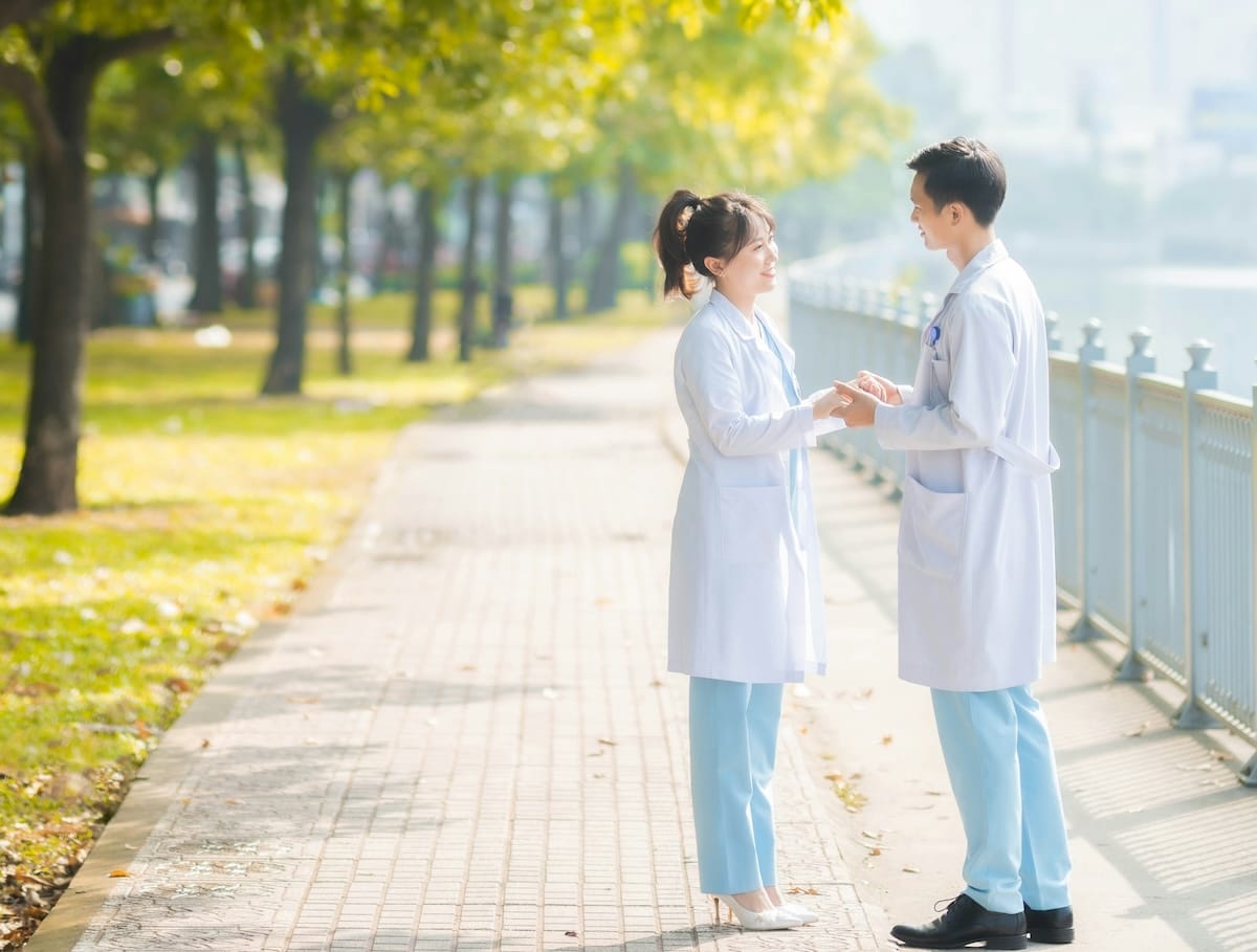 Two medical professionals outdoors standing together by a fence