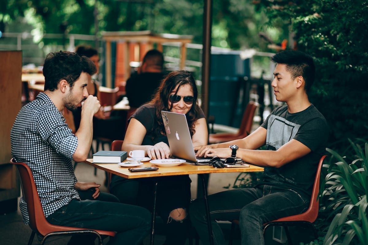 Group of three friends sitting outside at a table working on laptop computers
