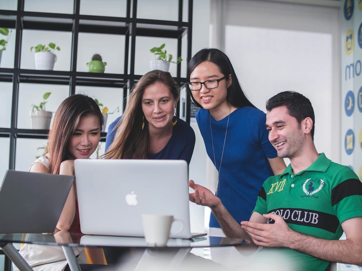 Group of four students gathered around a table and a laptop