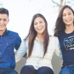 Group of five students sitting outdoors with a neutral backdrop