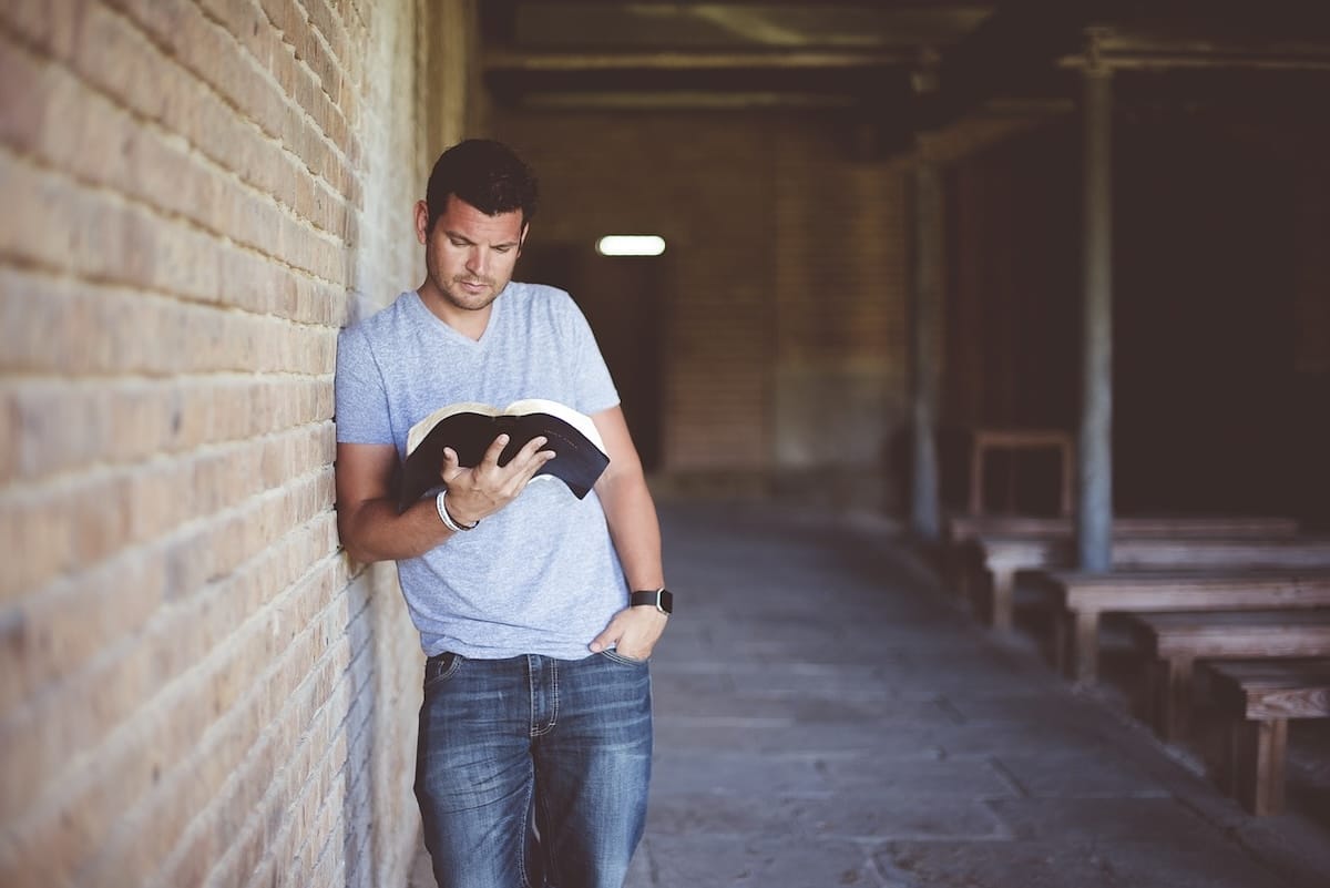 Individual standing outside beside a wall reading a book