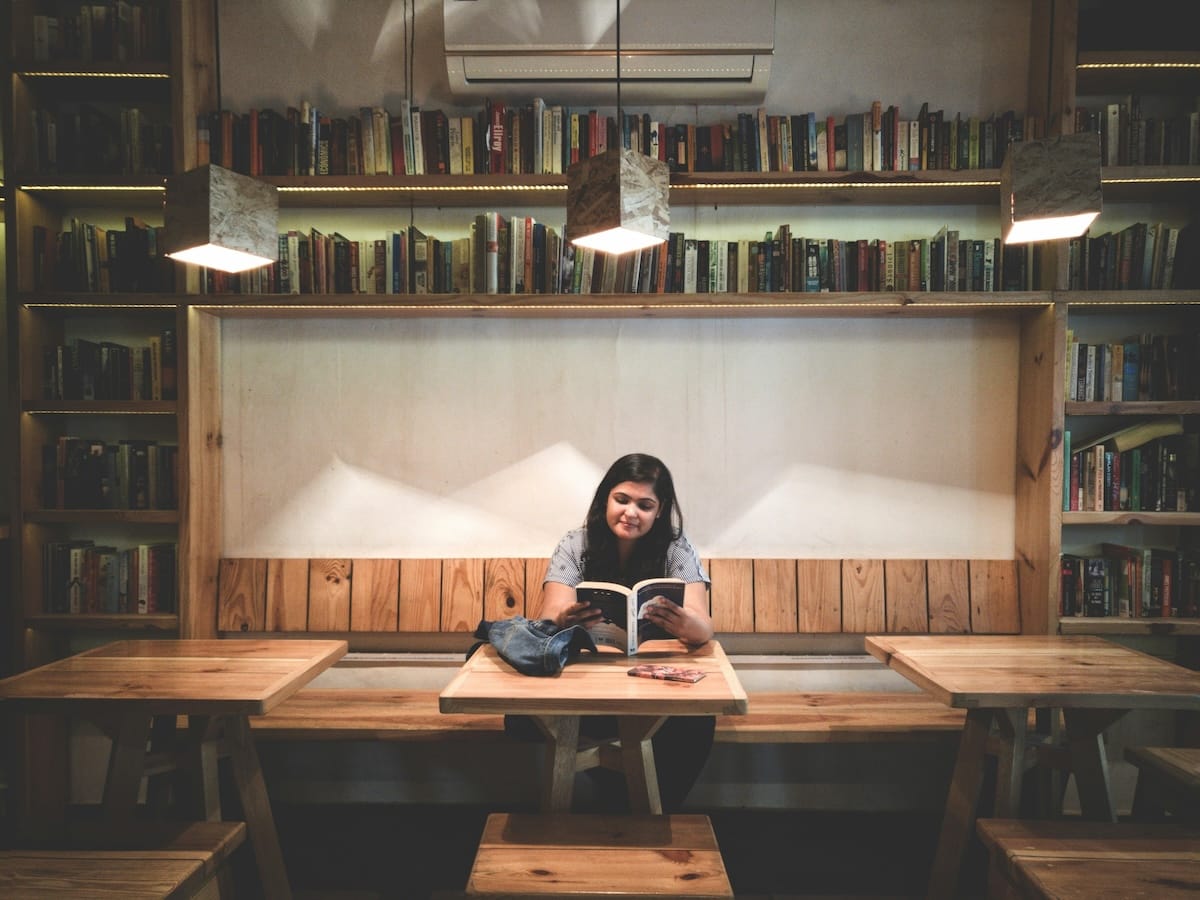 Individual sitting reading a book inside with bookcases and tables