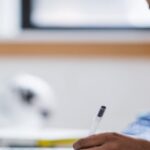 Individual student studying inside at a computer with pen and books
