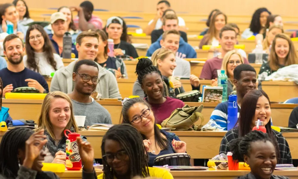 Individual sitting at a table with a laptop computer with notebooks and cup